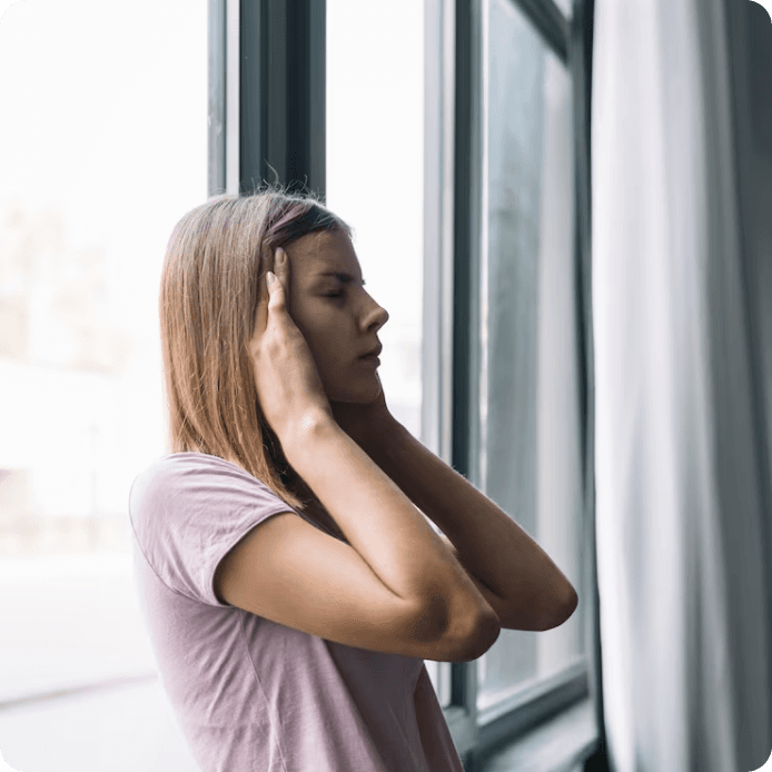 Kobieta przy oknie zatyka uszy przed hałasem